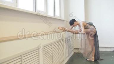 舞台服装的芭蕾舞者，在课堂上，在靠近窗户的垂直分割中伸展腿部